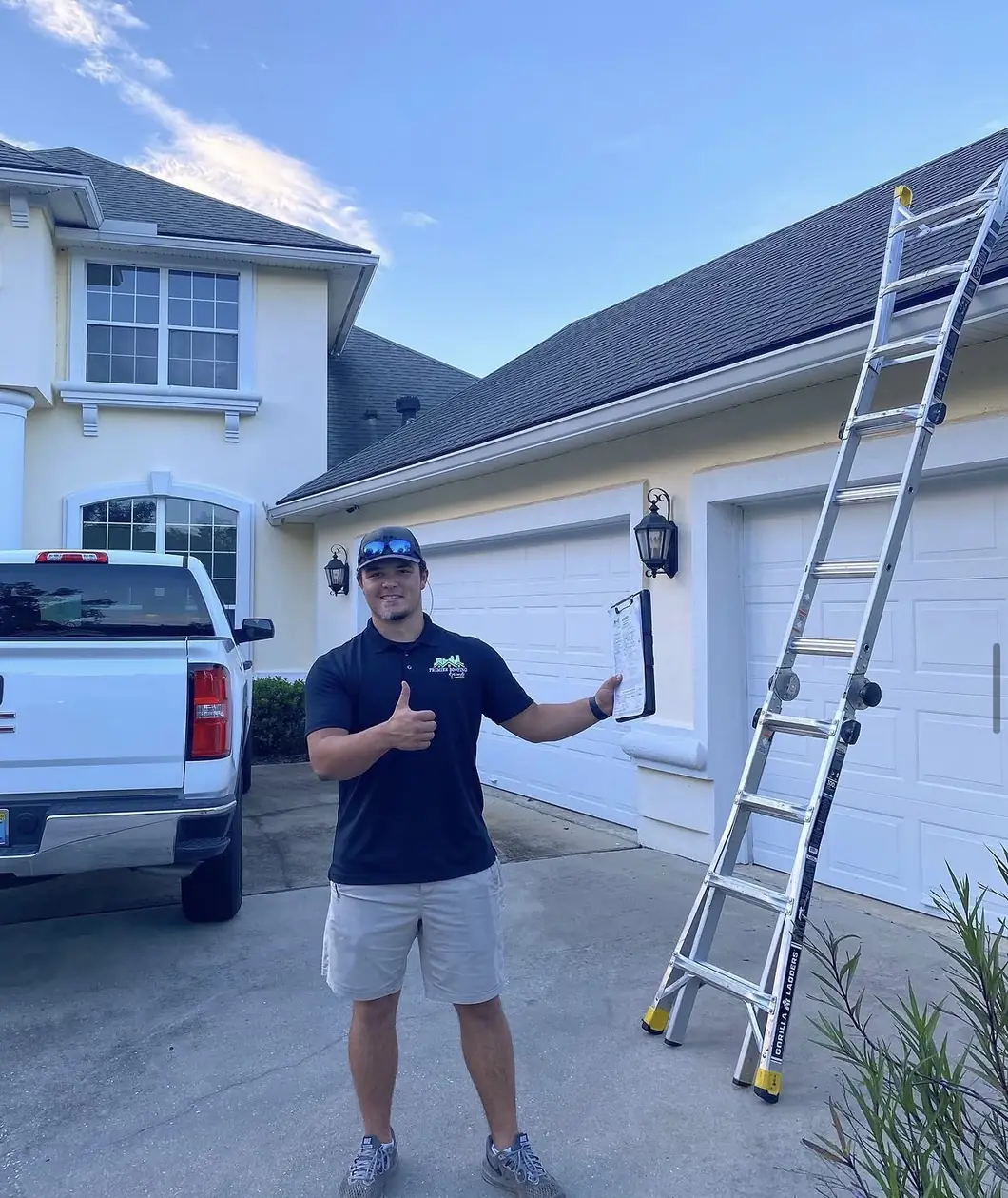 Premier Roofing team member giving a thumbs up beside a home with a shingle roof and roofing ladder